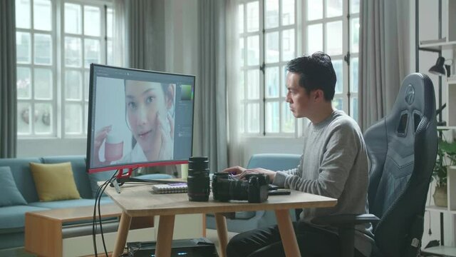 Asian Cameraman In Long Sleeved T-Shirt And Black Pants Using Desktop Computer For Editing Photos While Working At Home.
