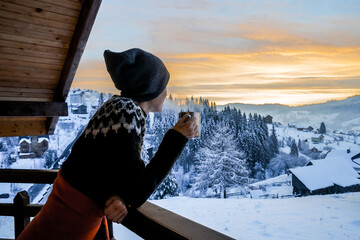 Young woman drinknig coffee or tea with a view of the winter mountain landscape