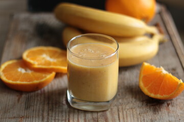 orange-banana smoothie in a transparent glass, on a wooden background