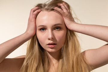 Fototapeta premium Young woman with blonde hair isolated on beige holding her head