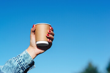 Woman hands holding a cup of coffee over blue sky background.