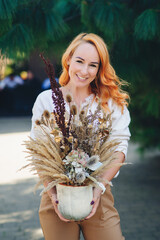 Florist holding stylish floral composition for autumn holidays. Bouquet of dried plants, flowers and autumn leaves.