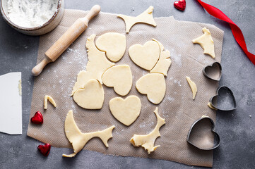 The process of cooking heart cookies. Top view of raw dough, rolling pin and baking cutters. Dark background