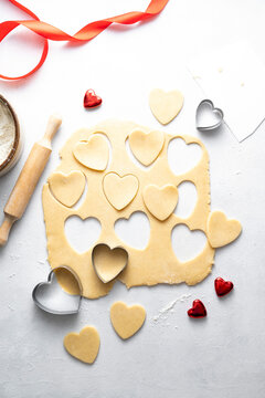 The process of cooking heart cookies. Top view of raw dough, rolling pin and baking cutters. Vertical image.