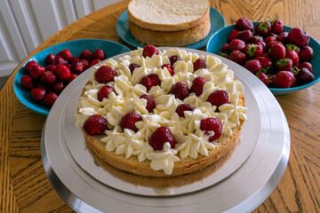 The process of making a biscuit cake is decorated with cream and strawberries.