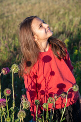 A smiling teenage girl with long hair. A girl in a red jacket in a summer field with flowers. The concept of walking outside - 482201362