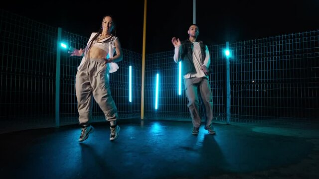 Professional dancers dancing hip hop outdoors. Youth culture. Modern choreography. Stylish dancers with neon lights at background. Slow motion. 4K, UHD
