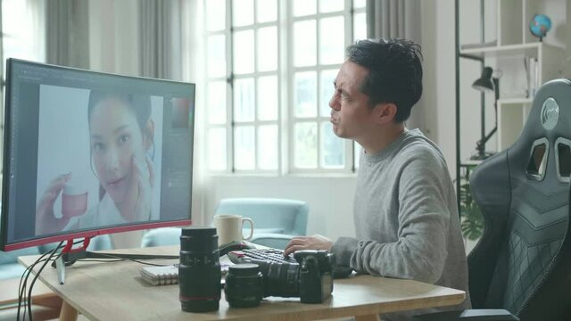 Asian Cameraman In Long Sleeved T-Shirt Having Backache While Using Desktop Computer For Working At Home.
