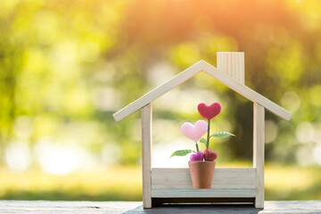 Flower of heart put in the wooden house model on sunlight in the public park, The buying a new real estate as a gift to family or the one loved concept.