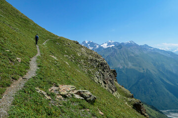 A male backpacker on a hiking trail leading to the Koruldi Lakes with an amazing view on the highlands and hills near Mestia in the Greater Caucasus Mountain Range, Upper Svaneti, Country of Georgia.