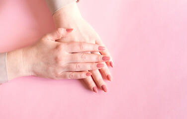 Fototapeta premium Female hands on a pink background. Beautiful well-groomed hands with classic manicure.