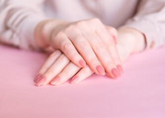 Naklejka premium Female hands on a pink background. Beautiful well-groomed hands with classic manicure.