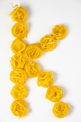 few homemade fettuccine nest in the shape of the letter K isolated on white background