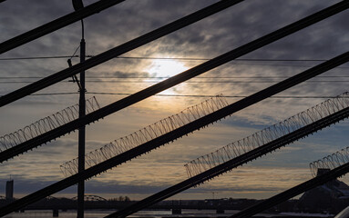 Fototapeta na wymiar barbed wire on bridge cables. sunlight between cloudy skies