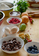 Preparation for cooking. There are beautiful plates of fruits and vegetables in bowls on the kitchen table. A sprinkle of chocolate on a plate.