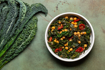 Sauteed kale, tomato and chickpea. Raw kale or leaf cabbage. Vegetarian dish. Green surface. Top...
