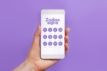 Mobile application on astrology with icons of zodiac signs. Woman holding mobile phone with...