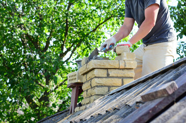 Repairing and rebuilding a brick chimney. A building contractor is rebuidling a chimney on a house...