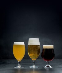 Three glass cups with different beers on a dark textural background.