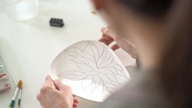 Asian woman design stylish pattern for painting self-made pottery plate with friends. Happy female enjoy leisure activity handicraft hobbies ceramic sculpture painting workshop at pottery studio.