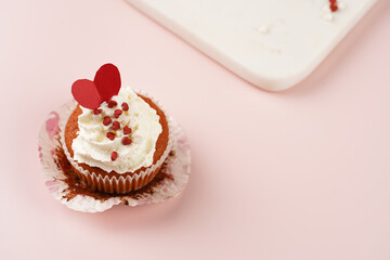 Three homemade white and chocolate muffins with white creamy frosting and heart-shared red and white sugar decoration on marble board on pink surface