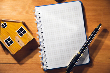  Blank notebook with house model on brown wooden background