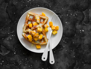 Sweet waffles with mango and dulce de leche  on a dark  background, top view