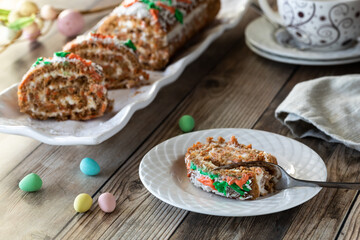 A serving of carrot cake jelly roll with a platter of the same in behind.