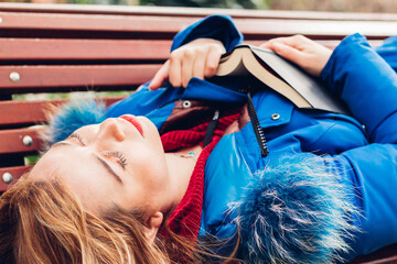 Woman in love lying on a park bench, holding a book of poetry or love novel, while sighing deeply...