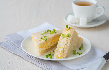 Tea sandwiches with egg salad on a white plate on a light concrete background. Sandwich recipes.