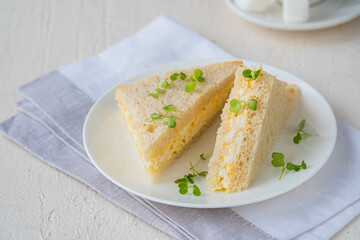 Tea sandwiches with egg salad on a white plate on a light concrete background. Sandwich recipes.