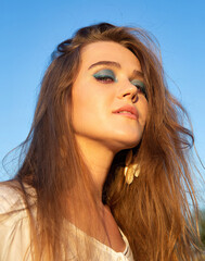 Portrait of young woman with white skin with sky behind with blue eyeshadow makeup
