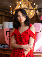 Irate young dark haired woman with white skin in restaurant in red dotted dress