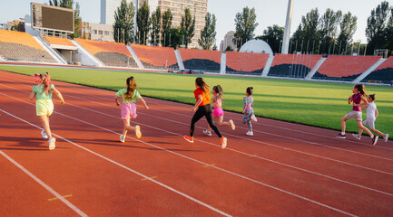 Fototapeta premium A large group of girls, are taught by a coach at the start before running at the stadium during sunset. A healthy lifestyle.