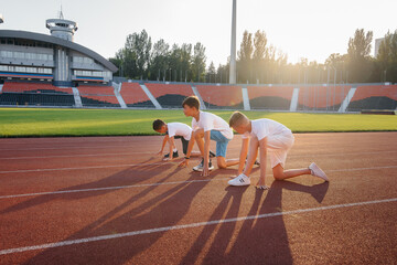 A large group of boys ' children are taught by a coach at the start before running at the stadium during sunset. A healthy lifestyle.