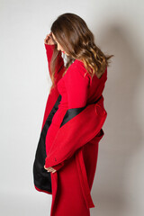 Fototapeta premium Looking away attractive young european woman standing isolated on light grey in red coat