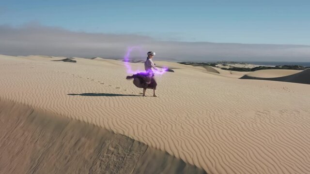 Aerial view of woman in Virtual Reality helmet and joysticks in desert nature is fighting or painting by creating colorful fire beams, and catching ultra violet electrical discharge. AR Immersive fun