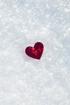 A red heart lies in the snow on a sunny day, a place for text