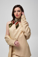 Pretty european woman with dark hair in beige suit with bright silk scarf isolated on light grey