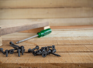 a set of black matte self-tapping screws on a wooden surface, selective focus in the foreground, abstract background, space for text, the concept of tools and repair work
