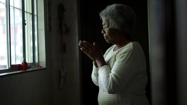 A contemplative senior black woman praying to God at home