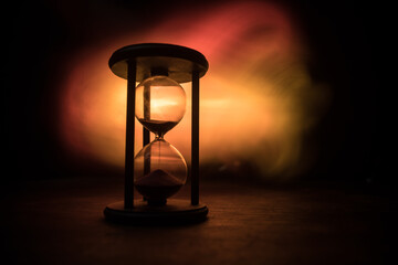 Time concept. Silhouette of Hourglass clock and old vintage wood clock with arrow and smoke on dark background with hot yellow orange red blue cold back lighting, or symbols of time with copy space