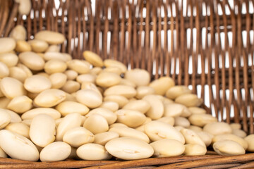 Lots of organic white beans in a vine basket, close-up, isolated on white.