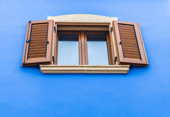 Window with a stone frame and doors with Mallorcan-style wooden slats. on the blue facade of a house.