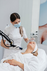 A young girl gets a carbon peeling for the skin of the neck in a beauty salon. Laser pulses cleanse the skin. Hardware cosmetology. The process of photothermolysis, warming the skin.