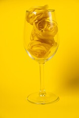 Raw fettuccine pasta in a wine glass isolated on yellow background