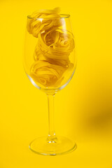 Raw fettuccine pasta in a wine glass isolated on yellow background