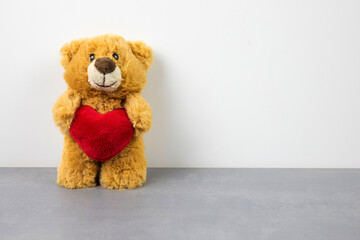 a teddy bear doll holding a heart-shaped pillow with love.
