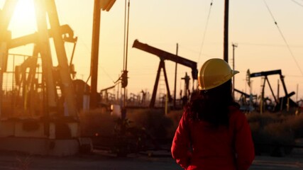 An Asian woman engineer inspects oil pumps at sunrise in a large oil field in California.