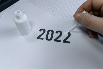 A man erases the year 2022 with correction fluid. The concept of the outgoing 2022